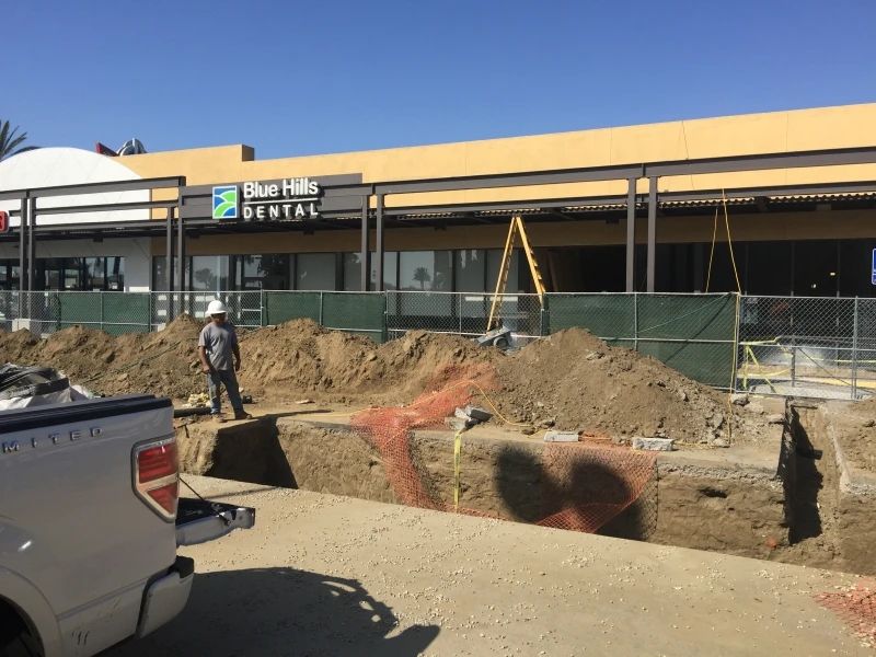 Construction site in front of a dental office. A worker stands near trenches, fenced off with dirt mounds and a truck.