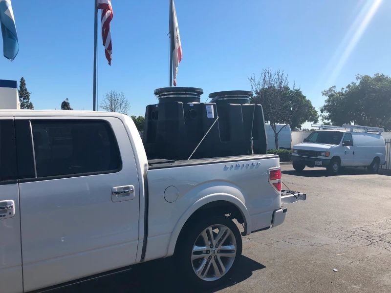 A white pickup truck carrying two black septic tanks. American and California flags in background.