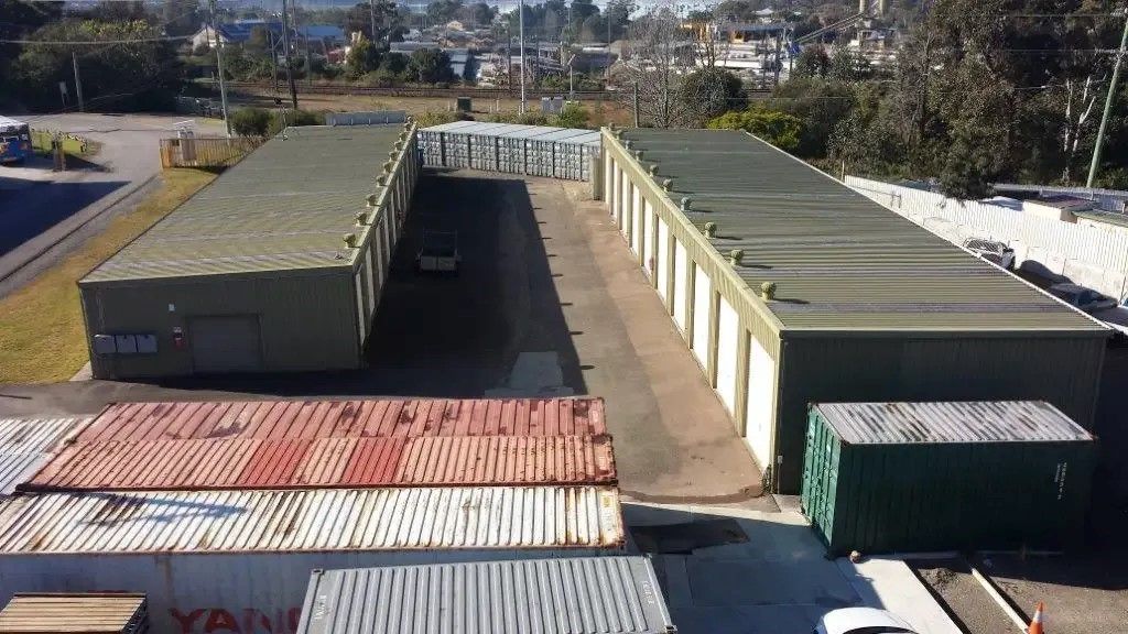 A Gray Metal Shed is Sitting in the Grass Next to a Bush — Teralba Business & Storage Park in Cardiff, NSW