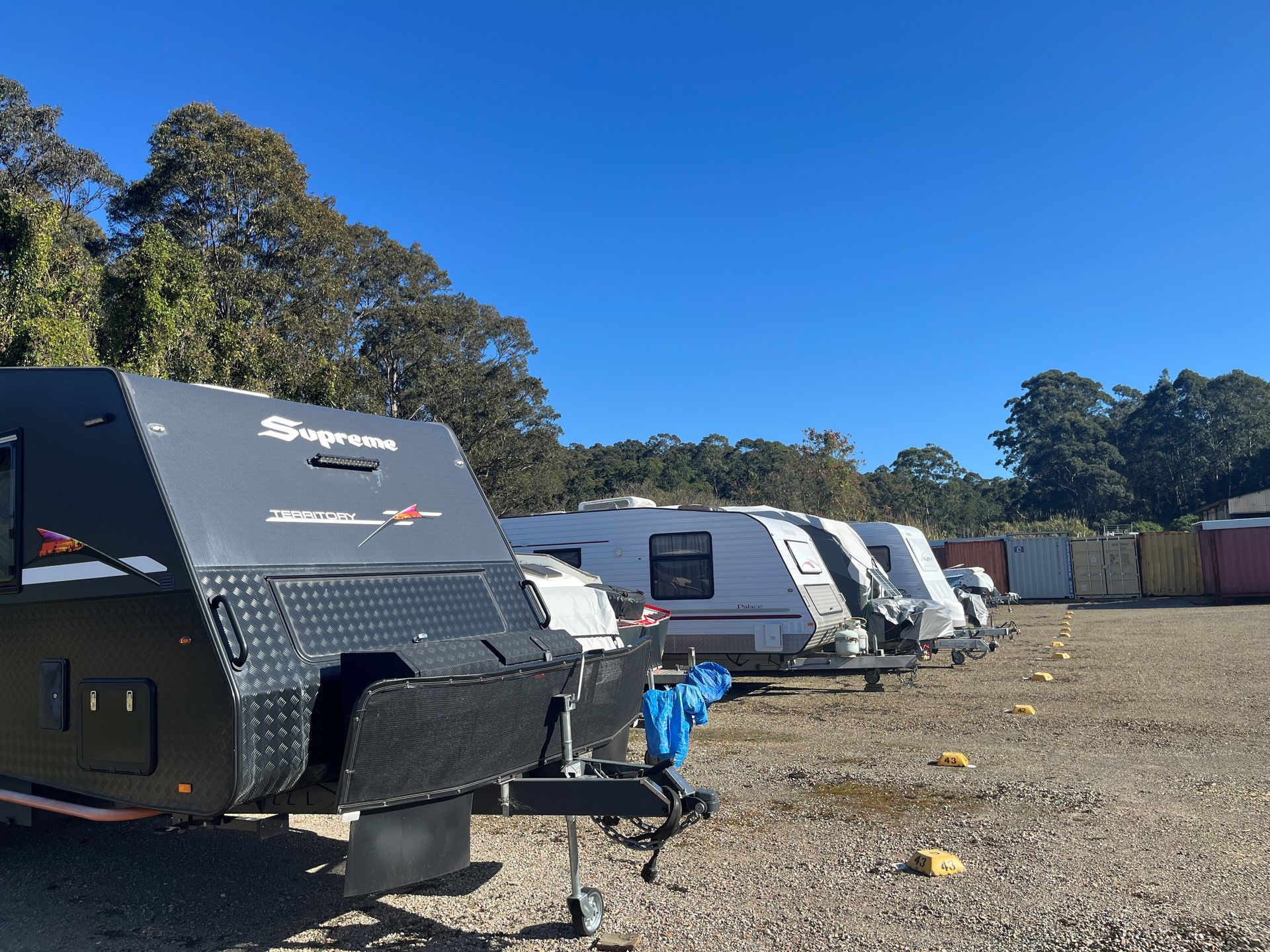 Row of caravans parked on gravel bays in an open lot under clear blue sky, each bay marked with yellow indicators.- Teralba Business & Storage Park in Toronto, NSW
