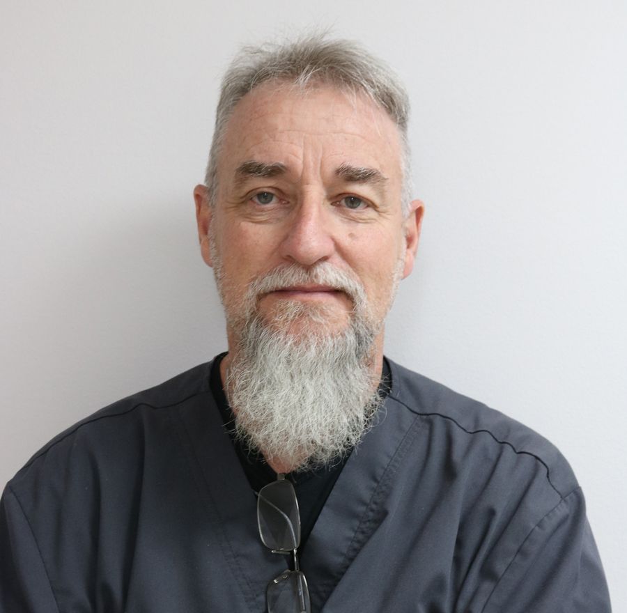 A man with a beard and glasses is wearing a scrub suit.