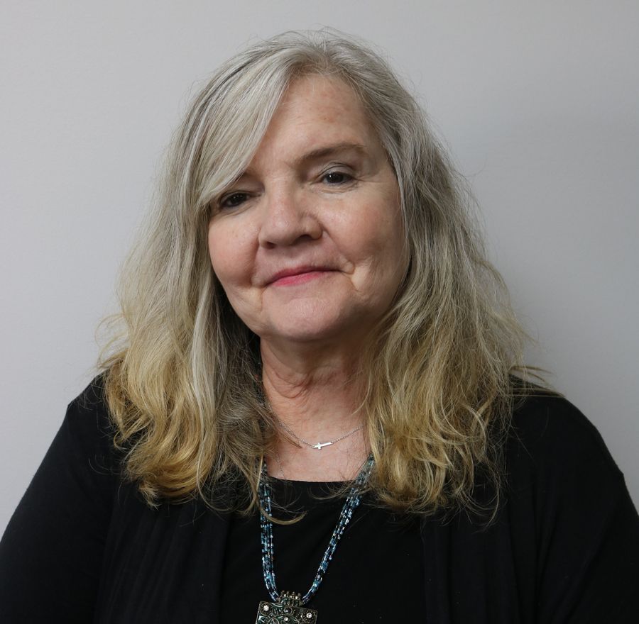 A woman with long blonde hair is wearing a black shirt and a necklace.