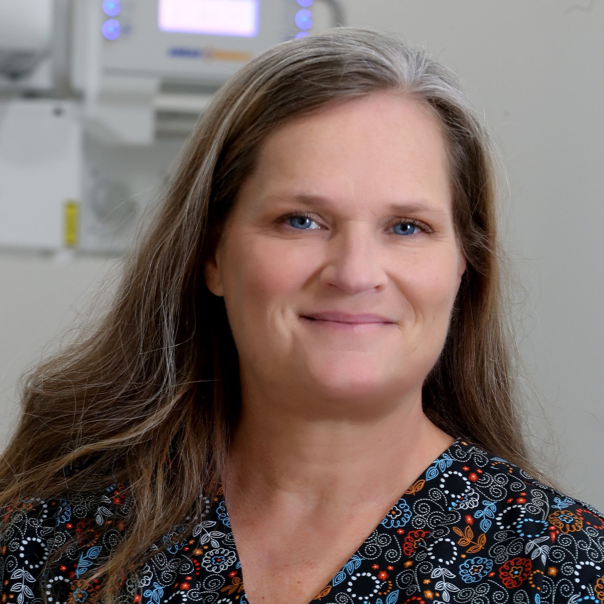 A woman in a scrub top is smiling for the camera.