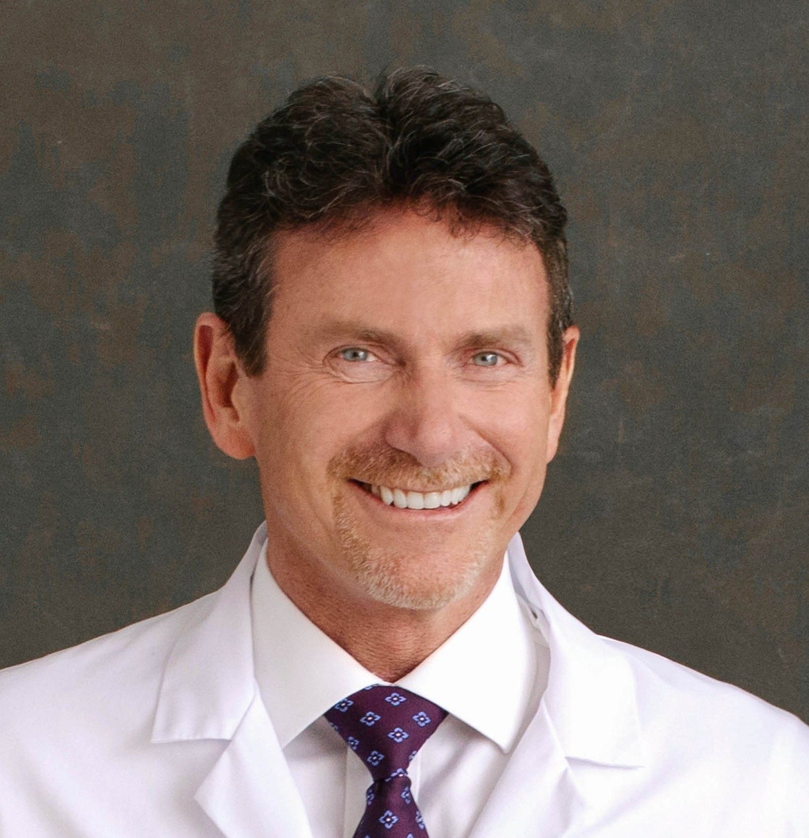 A woman in a white lab coat is smiling for the camera.