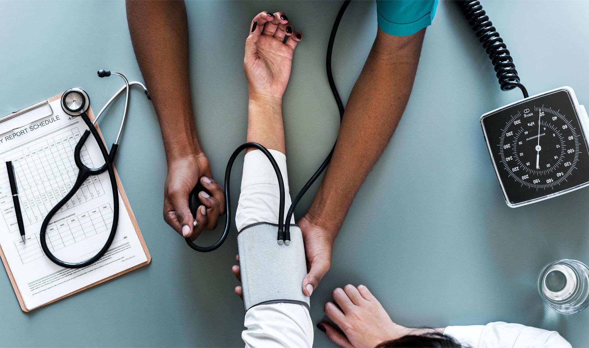 Healthcare worker checking a patient's blood pressure with a stethoscope and cuff on a desk