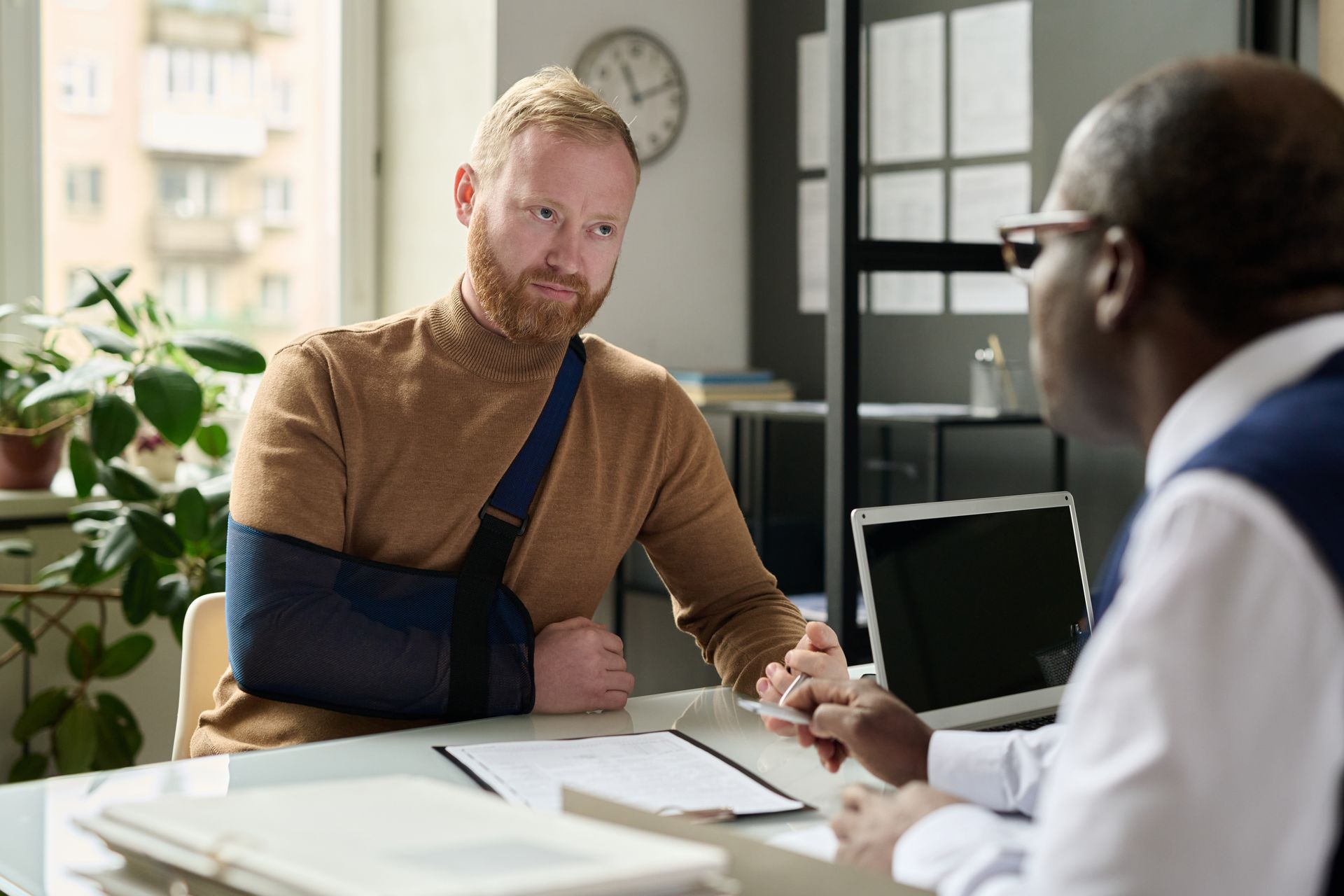 The lawyer consults the injured client, the desk cluttered with papers and a laptop. The lawyer consults the injured client, the desk cluttered with papers and a laptop.