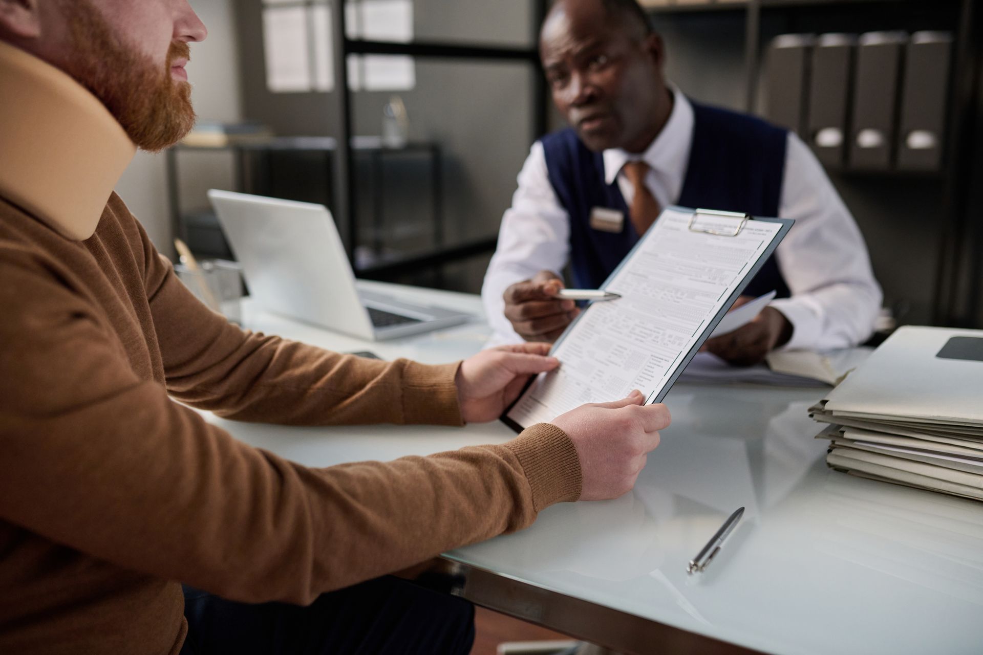 Close-up of a man with a neck brace holding legal forms applying for work compensation. Close-up of a man with a neck brace holding legal forms applying for work compensation.