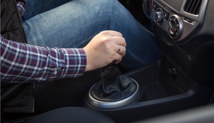Mano de una persona en la palanca de cambios de un automóvil, vestida con una camisa a cuadros y jeans, dentro de un automóvil.
