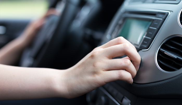 Mano girando el dial de la radio del coche. Vista interior.