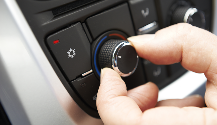 Mano girando el dial del aire acondicionado de un automóvil negro.