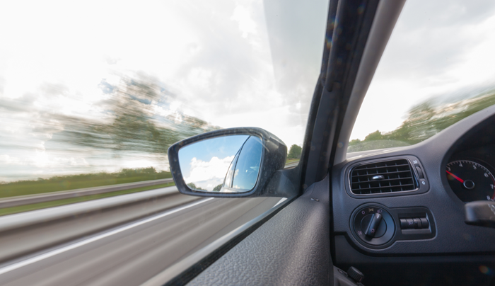 Vista desde el interior de un automóvil circulando por una autopista, fondo borroso y espejo lateral reflejando el cielo.