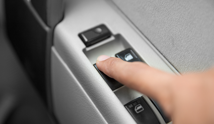 Dedo presionando el interruptor de control de la ventana de un automóvil en un panel de puerta gris claro.