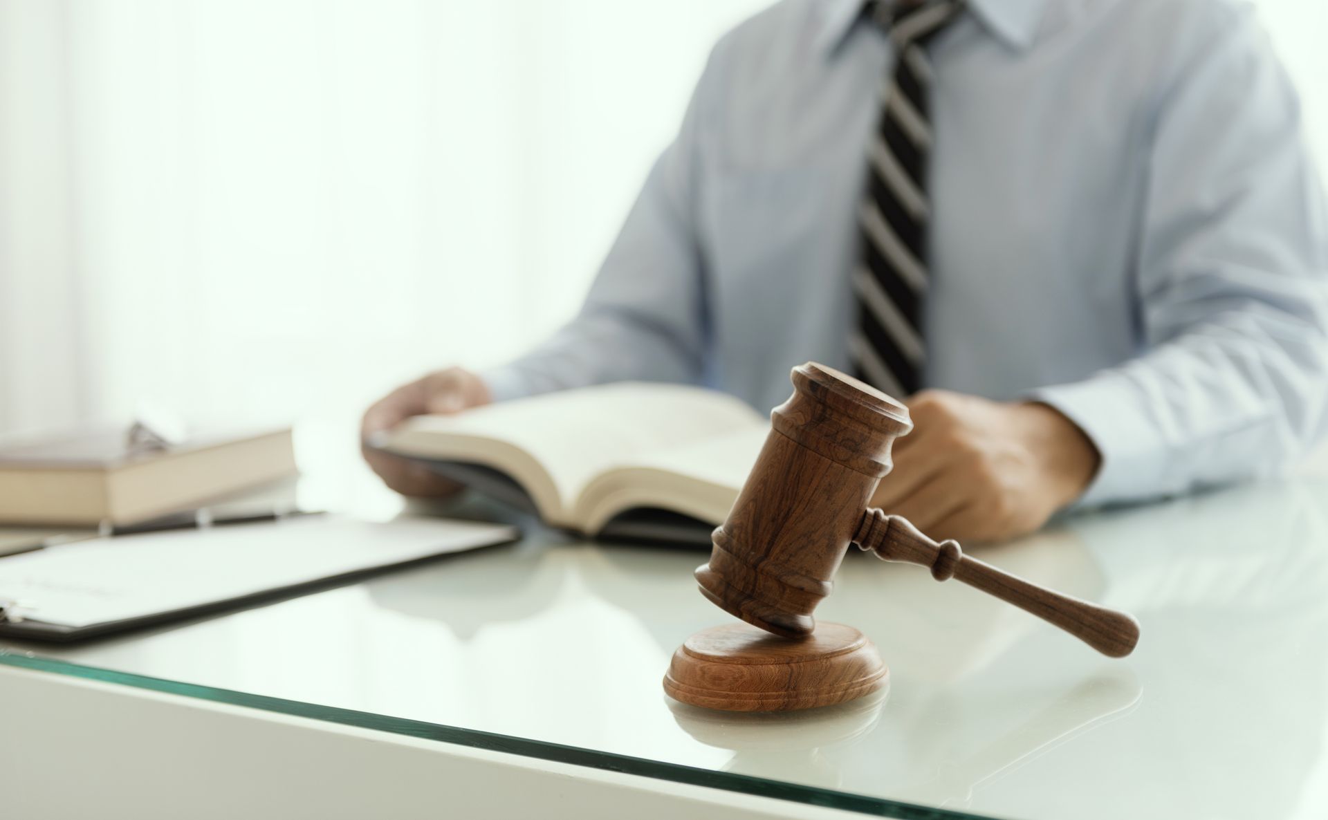 Gavel on desk, with person in shirt and tie reading a book.