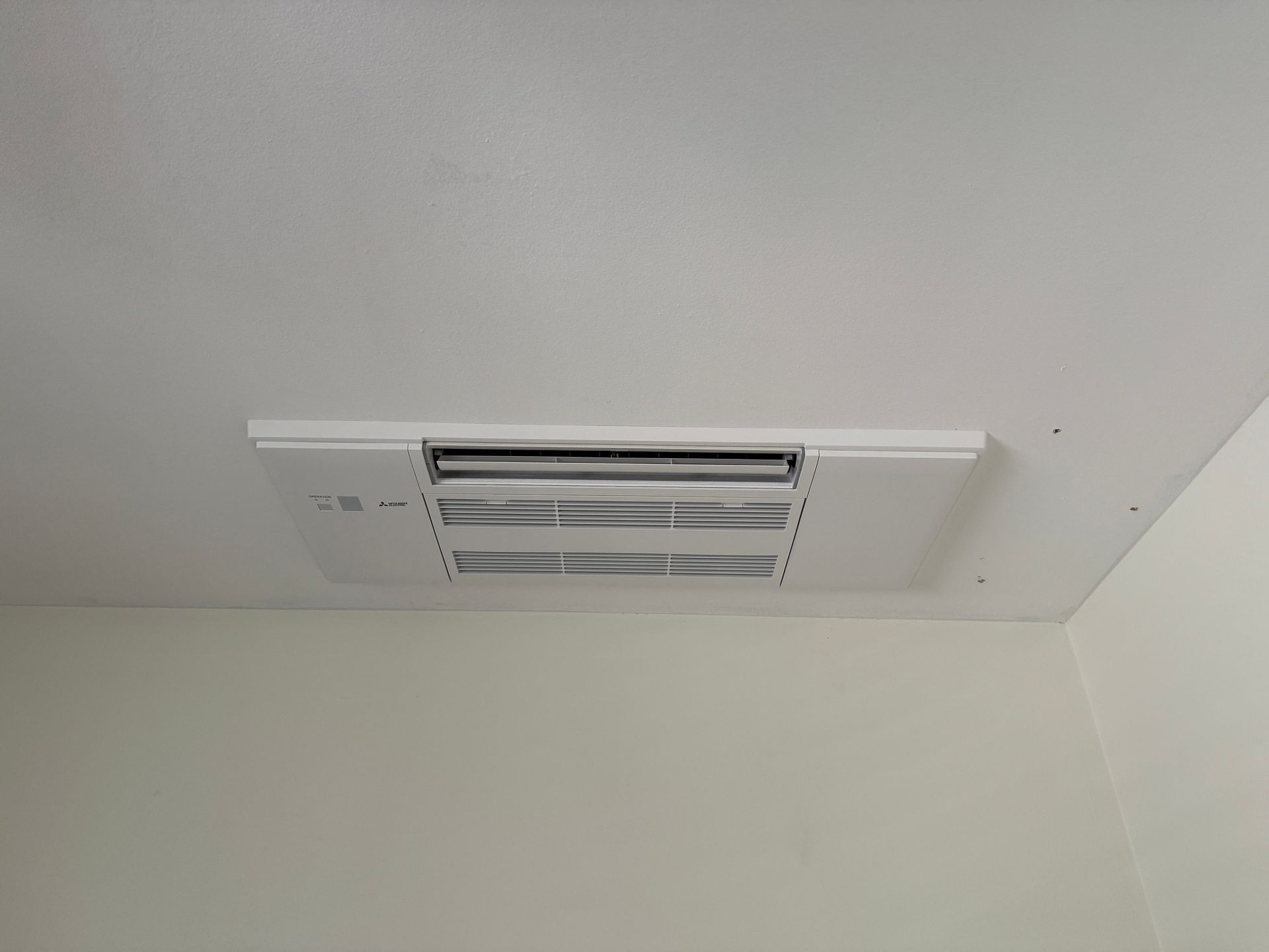 White ceiling-mounted air vent in a corner of a room with white walls.