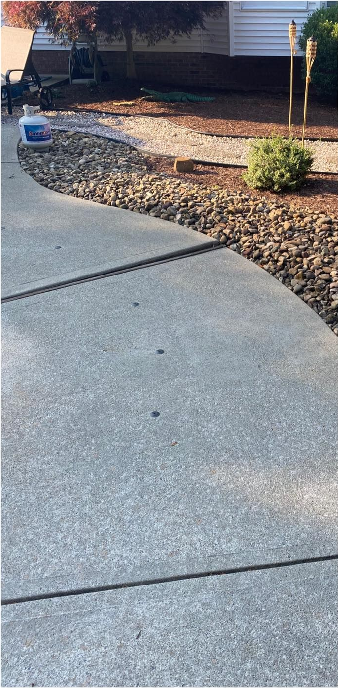 Concrete walkway curving past a rock garden and toward a house.