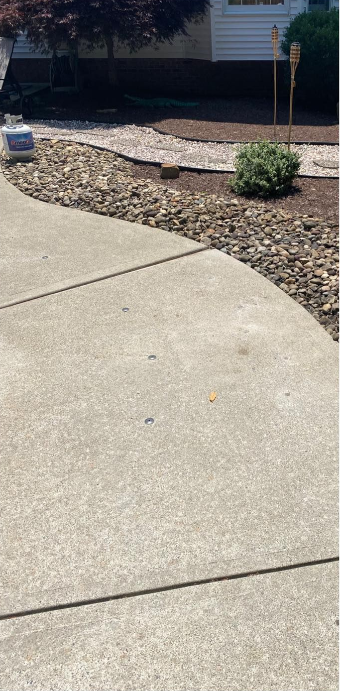 A concrete driveway curves past a rock garden with a small green bush and torch.