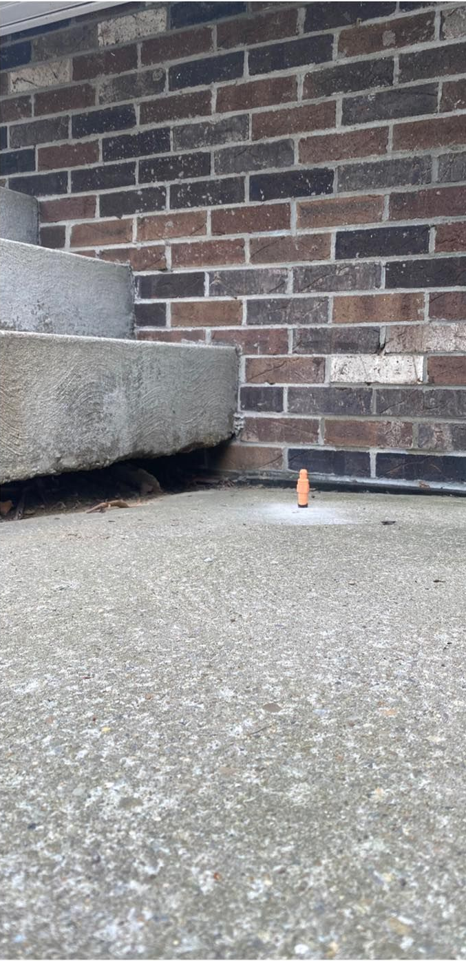 A small, orange, cone-shaped object on concrete surface near a brick wall and curved concrete structure.