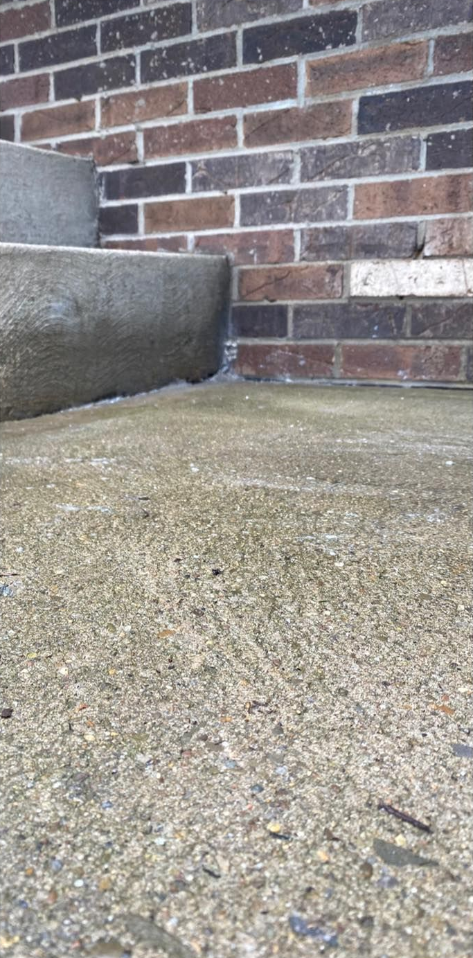 Concrete steps and ground next to a brick wall.