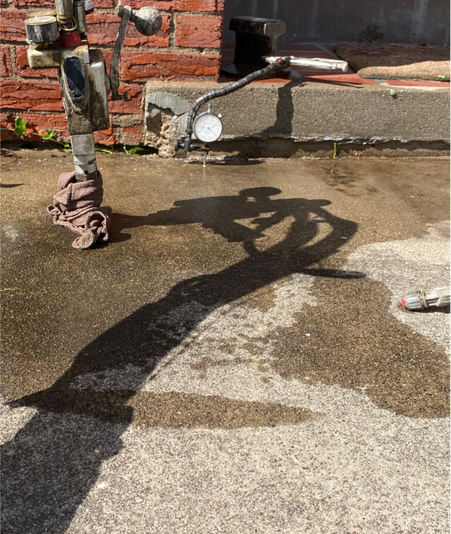 A water pipe with a pressure gauge on a concrete surface, casting a long shadow on a sunny day.