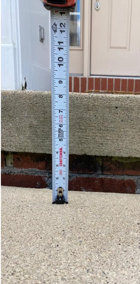A tape measure measuring the height of a concrete step, with brick beneath.
