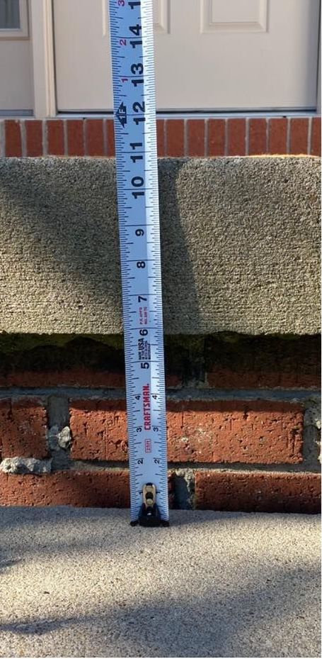 A measuring tape shows the height of a step. It measures approximately 8 inches from the concrete to the brick.