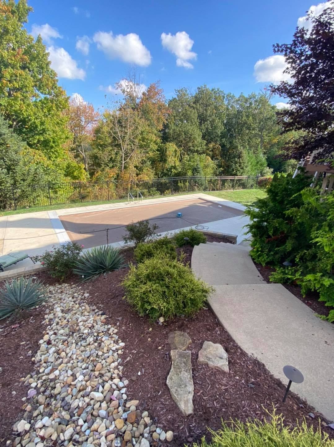 Landscaped yard with a covered pool surrounded by trees and a concrete pathway.