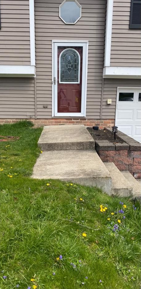 A house with a red door and a concrete pathway with steps leading to it. Lush green grass.