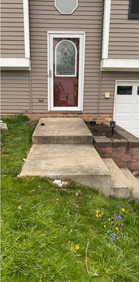 Exterior of a house with steps leading to a door; grass and landscaping in front.