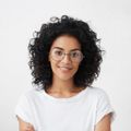 A woman with curly hair is wearing glasses and a white shirt.