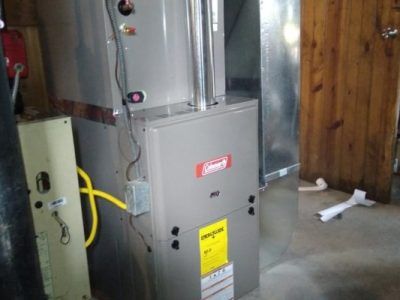 A coleman air conditioner is sitting in a room next to a wooden wall.