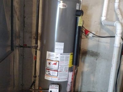 A water heater is sitting in a basement next to pipes.