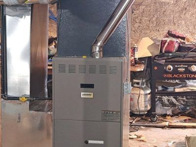 A furnace is sitting in a garage next to a grill.