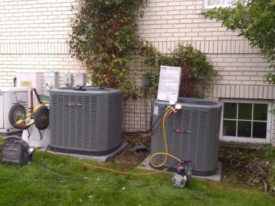 Two air conditioners are sitting on the grass in front of a brick building.