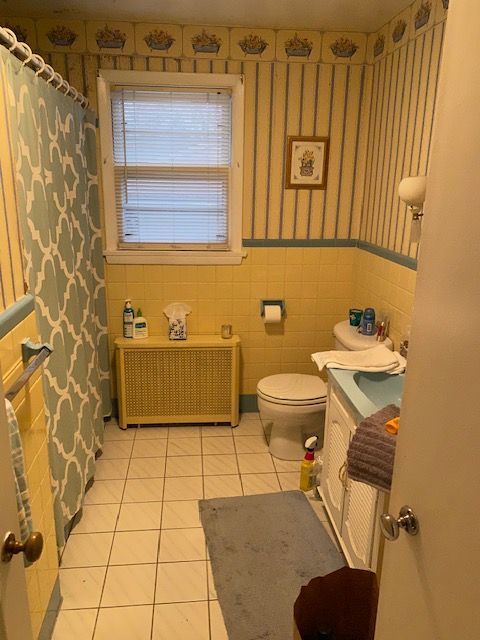 Bathroom with yellow and blue striped wallpaper, shower curtain, and tile.