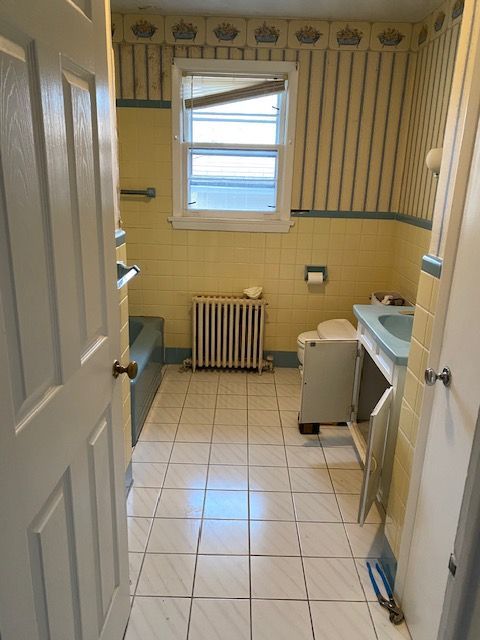 Bathroom with yellow tile and wallpaper, a radiator, and a blue sink.