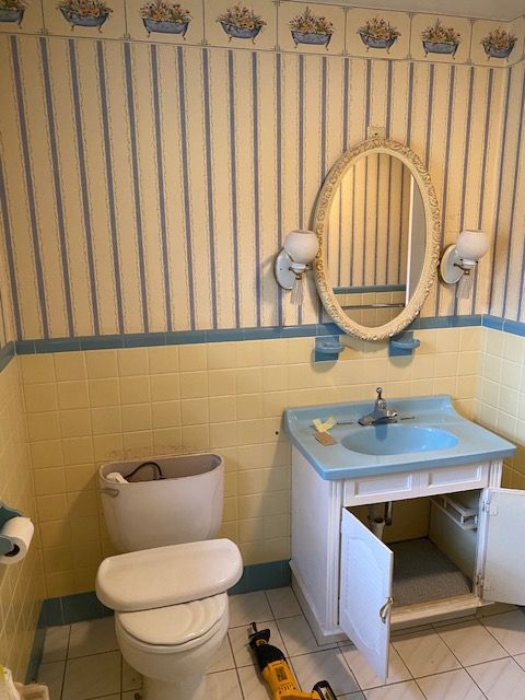 Bathroom with yellow and blue walls, white toilet, blue sink, mirror, and open cabinet.