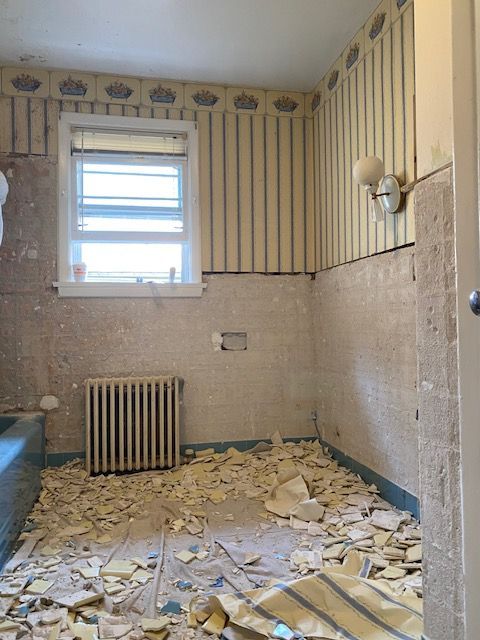Bathroom under renovation, with wallpaper, exposed wall, radiator, and debris on floor.
