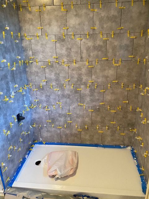 Shower stall with gray tiles, many yellow tile spacers, and white shower base.