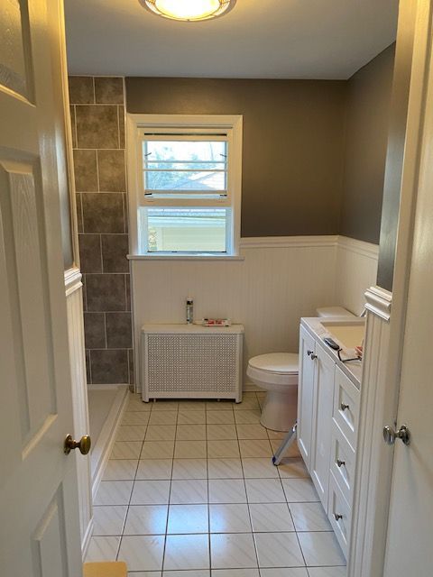 Bathroom interior with white tile floor, white wainscoting, gray wall, white vanity, and toilet.
