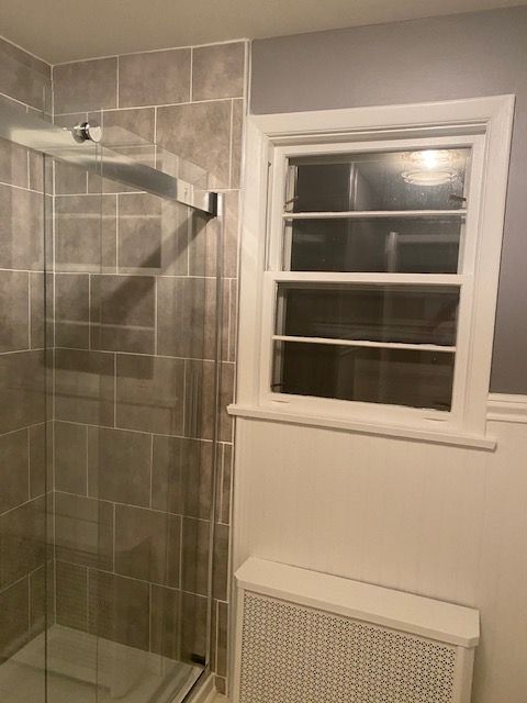 Bathroom with a tiled shower, window, and radiator. Gray and white color scheme.