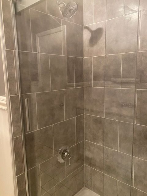 Shower with gray tiled walls, glass door, and silver shower fixtures.