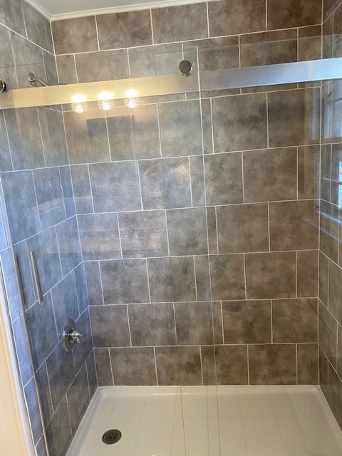 Tiled shower with a glass door, silver fixtures, and a white base. Walls are gray.