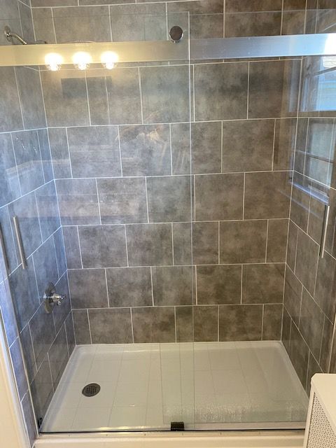 Gray tiled shower with a white base and sliding glass doors.
