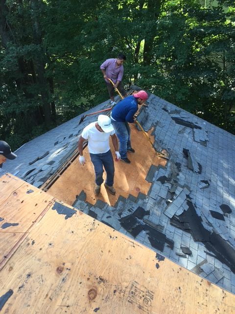 Roofers removing old shingles from a house roof on a sunny day.