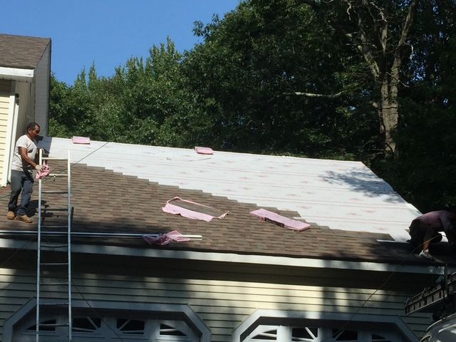 Roofers installing shingles on a house roof on a sunny day.