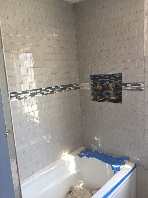 Gray tiled shower enclosure with a horizontal accent stripe and recessed shelf above a bathtub.