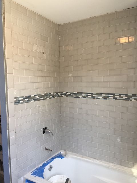 Bathroom with light gray subway tile walls, decorative border, and white bathtub.