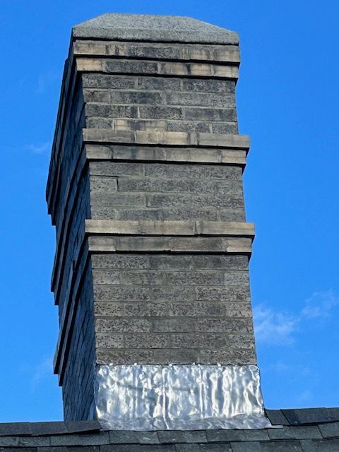 Brick chimney on a dark roof against a blue sky.