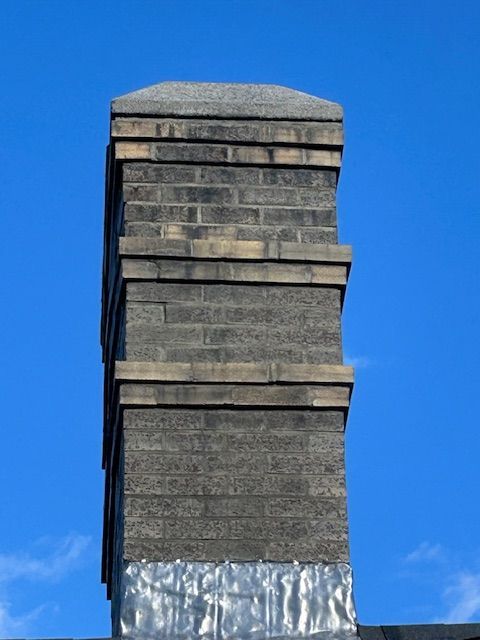 Brick chimney on a blue sky background. The chimney has decorative banding and a flat top.