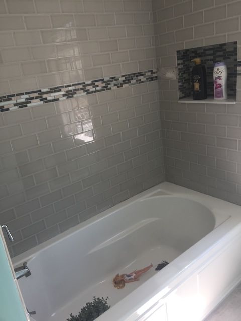 White bathtub with gray tiled walls, decorative accent strip, and built-in shelf.